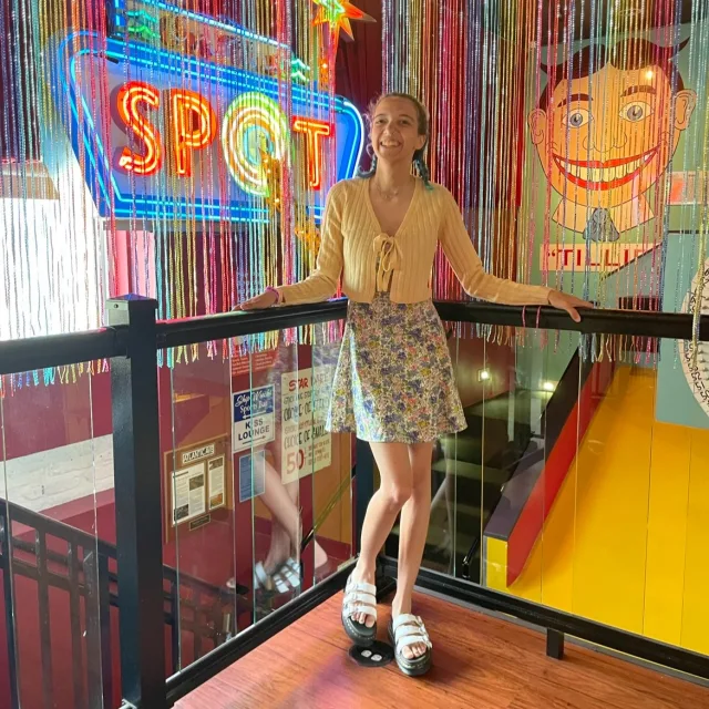Travel Advisor Madeleine Gossard standing in front of rainbow streamers wearing a yellow top and a floral skirt.