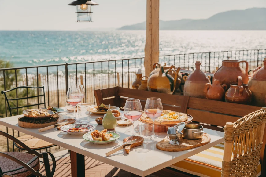 a seaside wooden table filled with wine glasses and colorful food