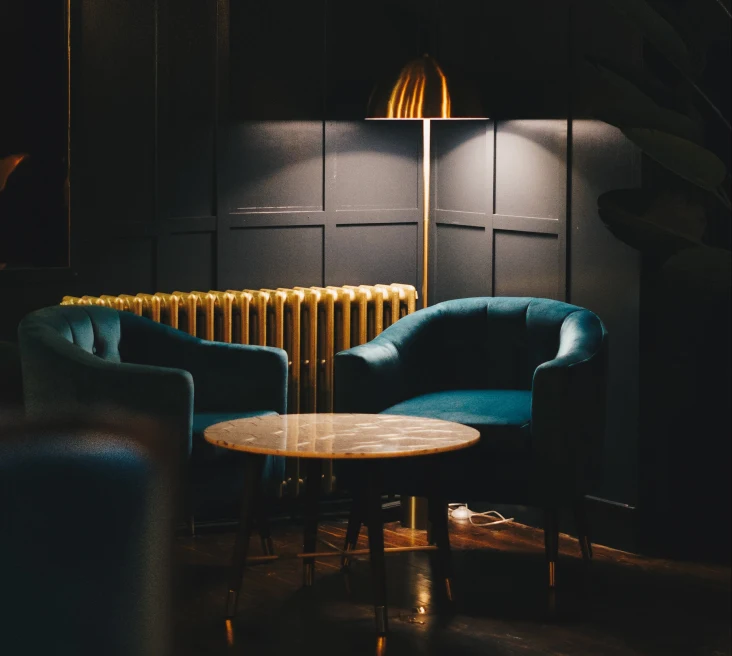 Two blue chairs with a wooden table in a dimly lit room with black walls