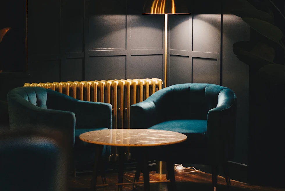 Two blue chairs with a wooden table in a dimly lit room with black walls