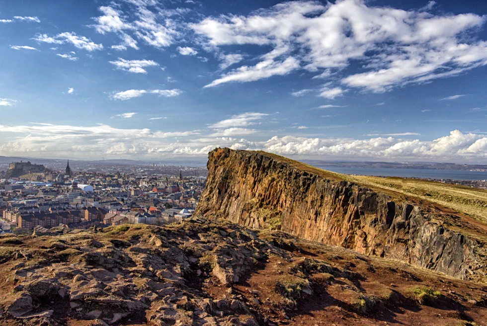 A grassy mountain with Edinburgh city in the background.
