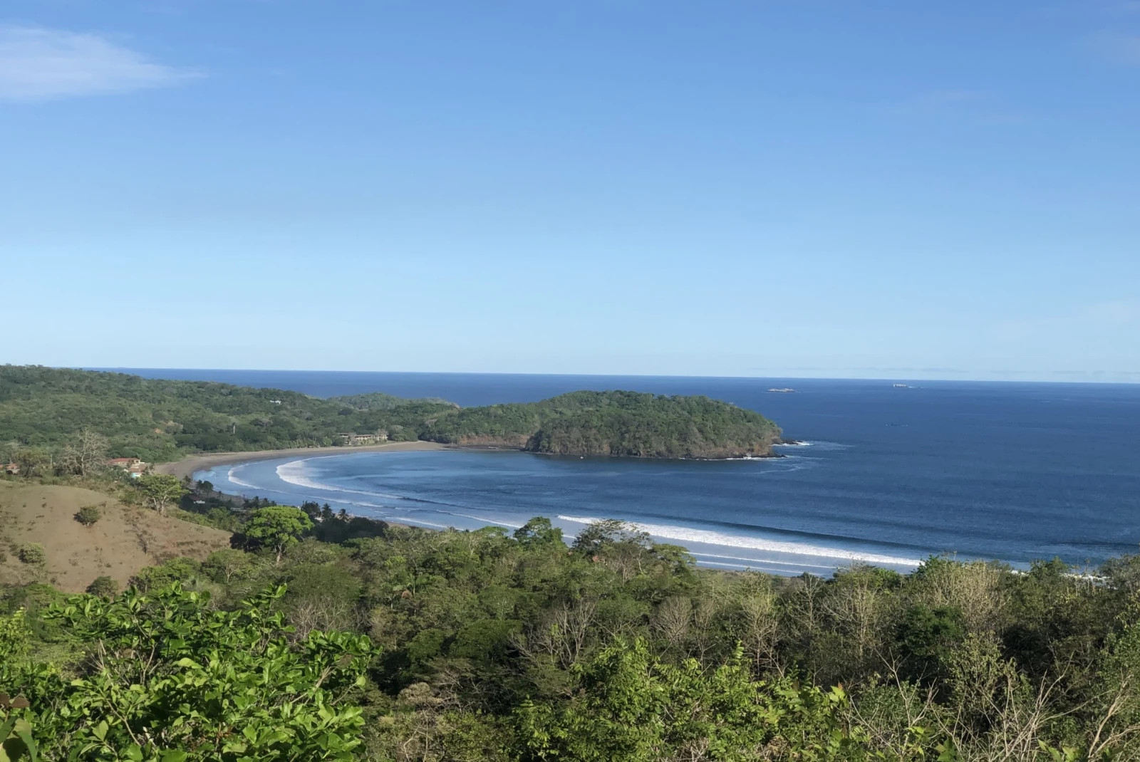 view from the top of hill of a beach cove with blue skies 
