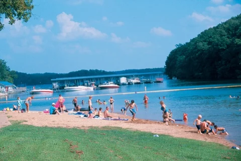 People enjoying the lake shore with boats in the distance and a clear sky.