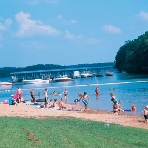 People enjoying the lake shore with boats in the distance and a clear sky.