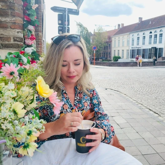 Travel Advisor Kara Winarksi wears a floral shirt and holds a coffee cup on a white table cloth with flowers beside her