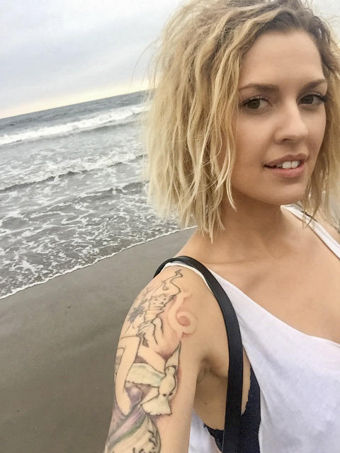 Selfie of a blond woman standing in front of the beach