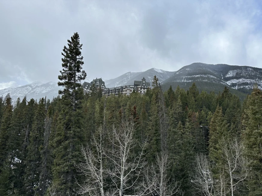 a lodge hotel at the top of a tree covered mountain, with snowy mountains in the distance on a cloudy winter day
