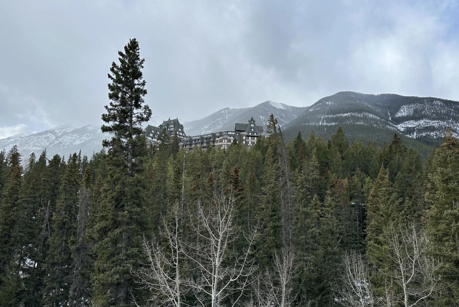 a lodge hotel at the top of a tree covered mountain, with snowy mountains in the distance on a cloudy winter day
