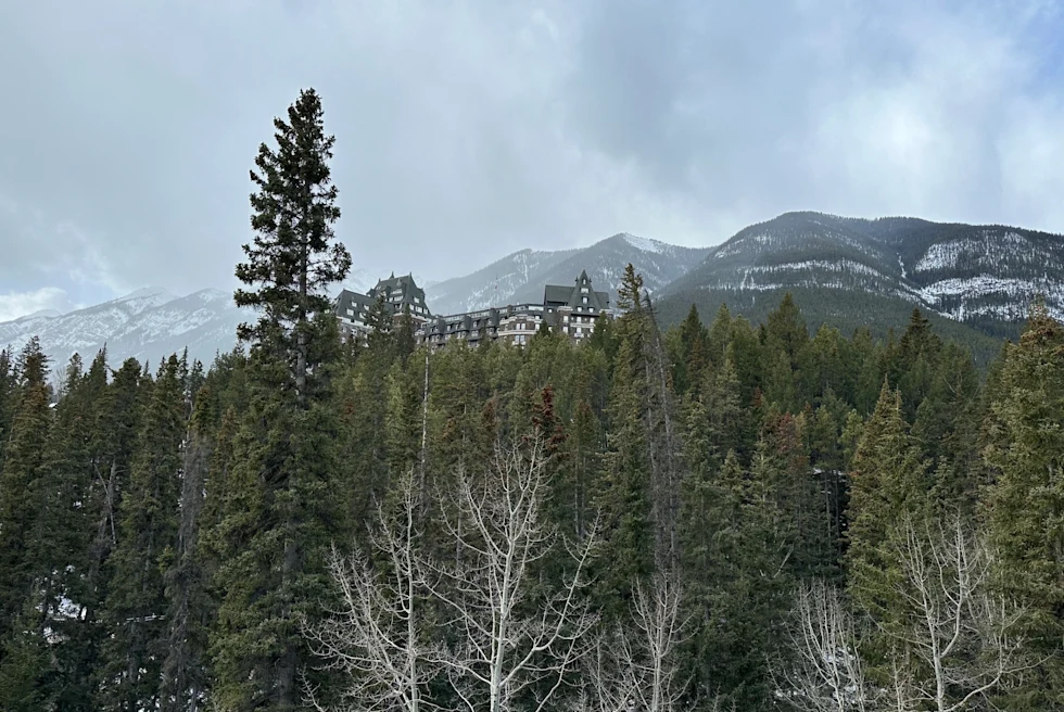 a lodge hotel at the top of a tree covered mountain, with snowy mountains in the distance on a cloudy winter day