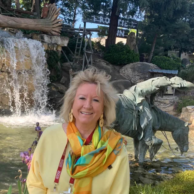 Travel Advisor Deborah Reeder in a yellow sweater and scarf in front of a fountain with statues.