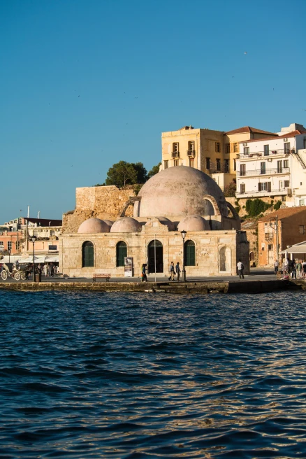 blue water and skies with white and tan ancient rounded buildings and a green leafy tree Crete old city Heraklion