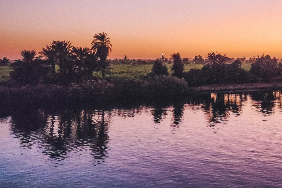 The Nile River at sunset with palm trees on the banks.