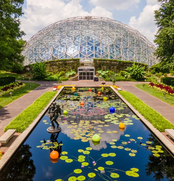 A view of a lily pad pond with beautifully manicured lawns, pathways and an elaborate glass dome in the center of the image. 