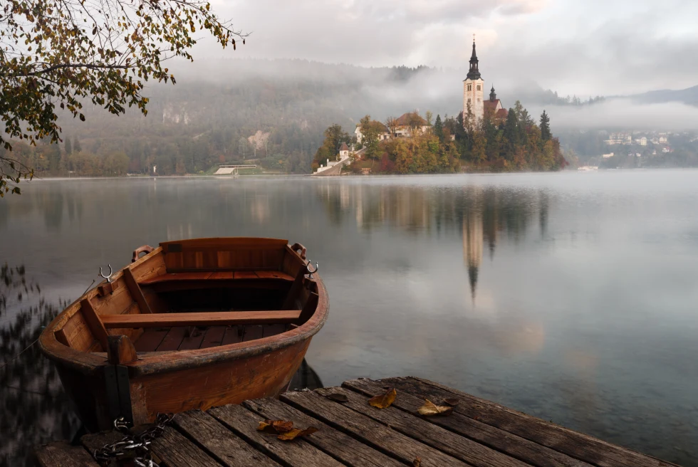 An island in the center of Lake Bled posted by a wooden boat.