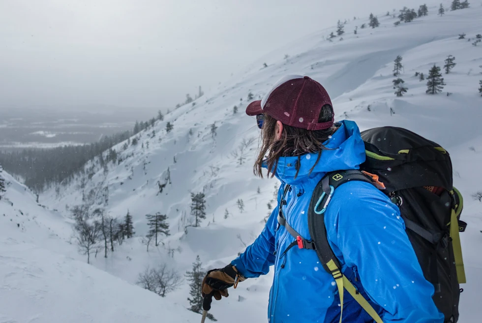 Girl in blue jacket with black backpack skiing down a slope.