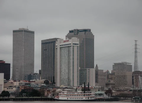 A view of a New Orleans Jazz Cruise on the river with skyscrapers in the background, on a cloudy day.