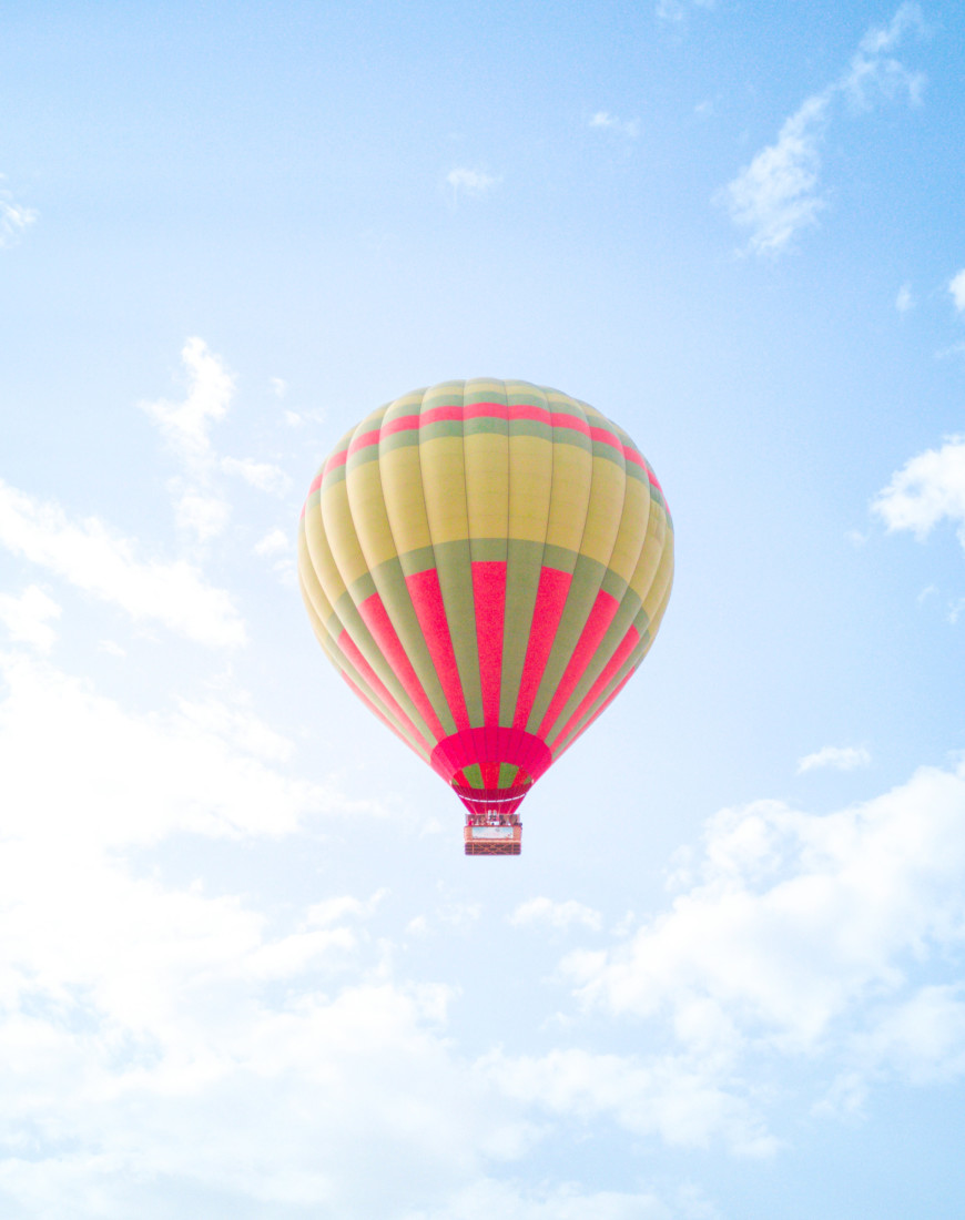 a pink, green, and yellow hot-air balloon in a light-blue sky