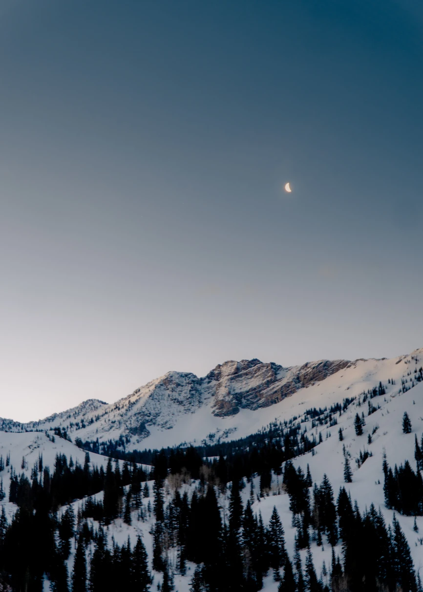 snow-covered mountain with the moon in the sky during sunrise