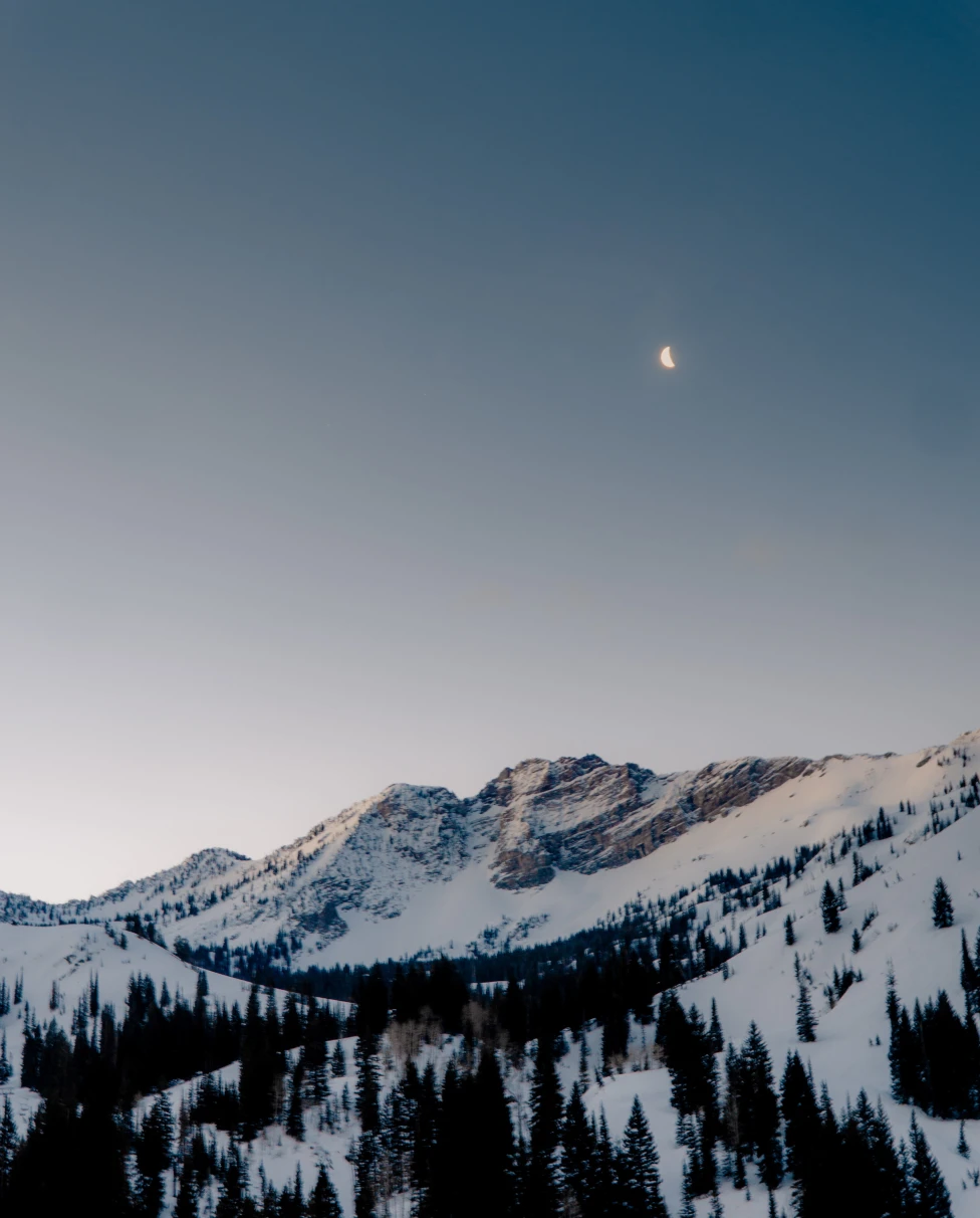 snow-covered mountain with the moon in the sky during sunrise