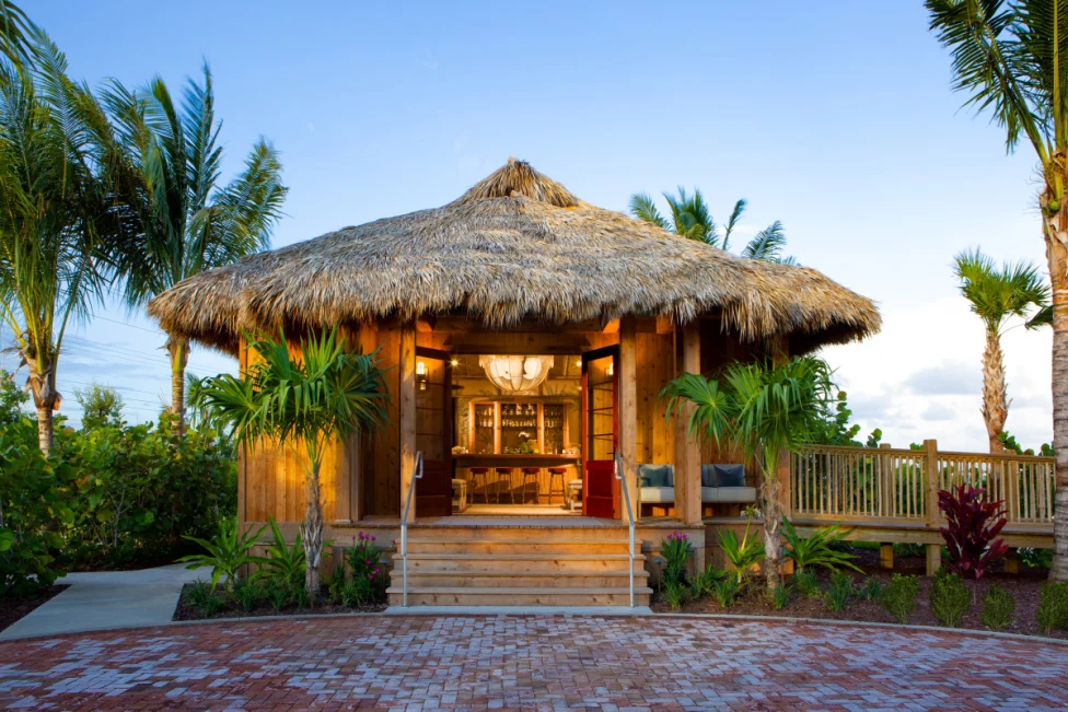 A beach hut with a bar inside and palm trees surrounding.