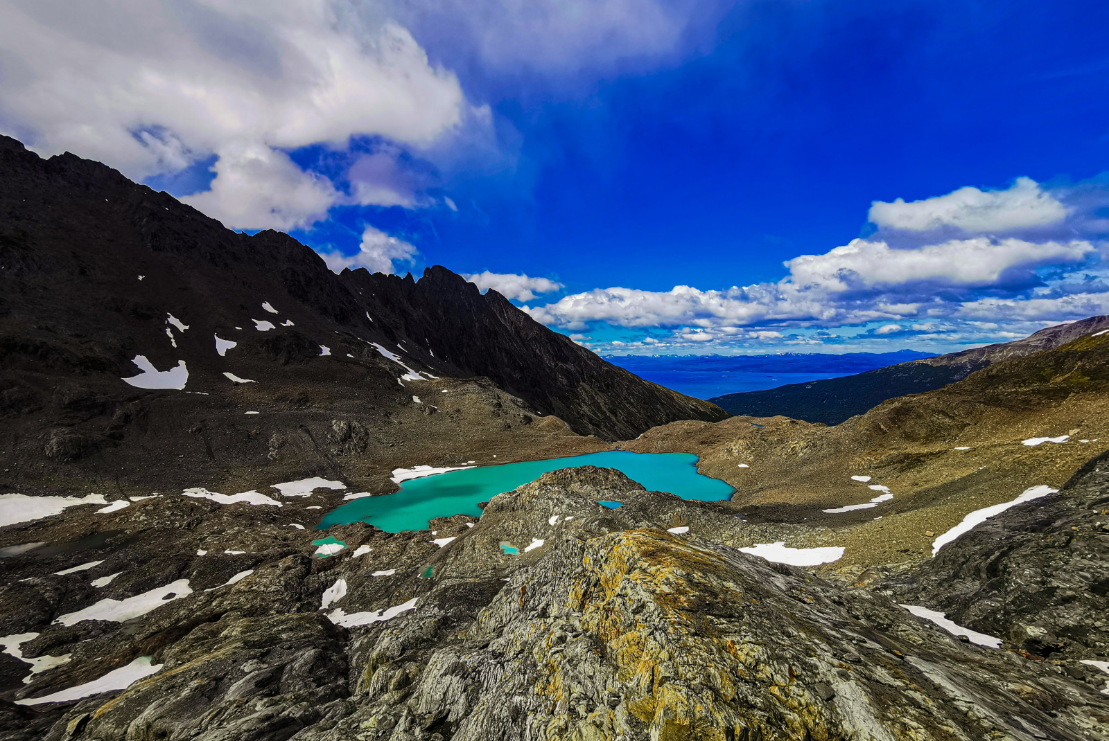 Tierra del Fuego National Park in Argentina with grey rock covered in green moss overlooking a jade blue crater lake in a sweeping valley. 