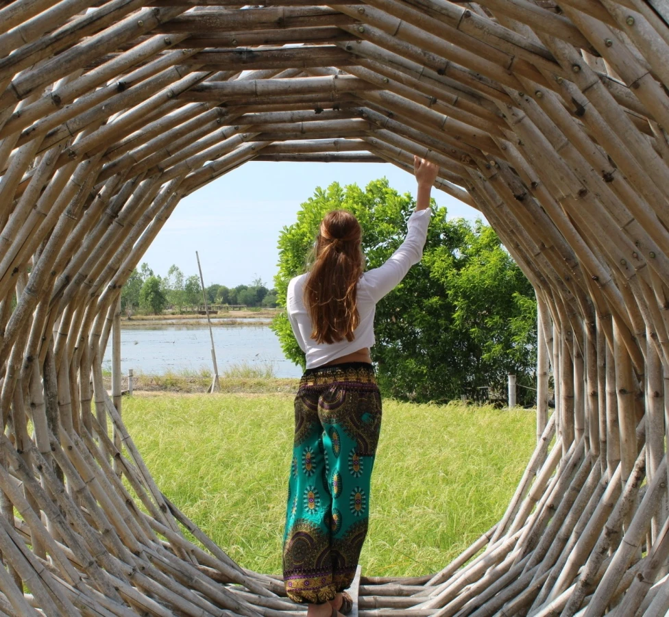 A person stands inside a circular wooden structure, gazing at a serene natural landscape.