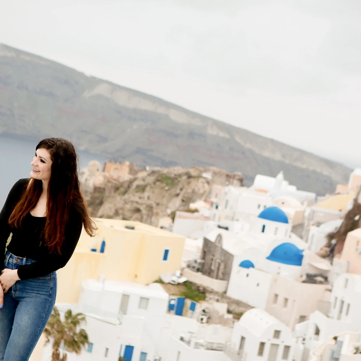 A woman in a black shirt and blue jeans standing on the seaside with a city view