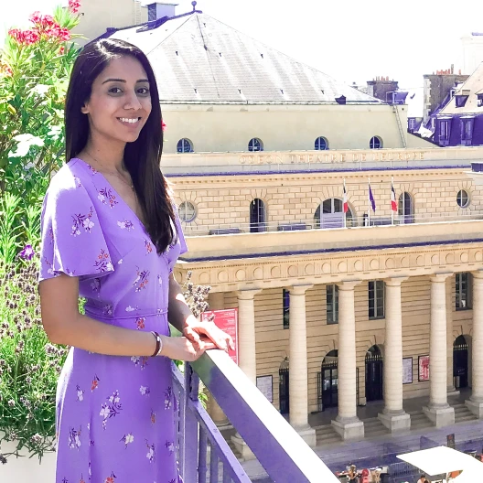 Shrinal in purple dress posing in front of a building.