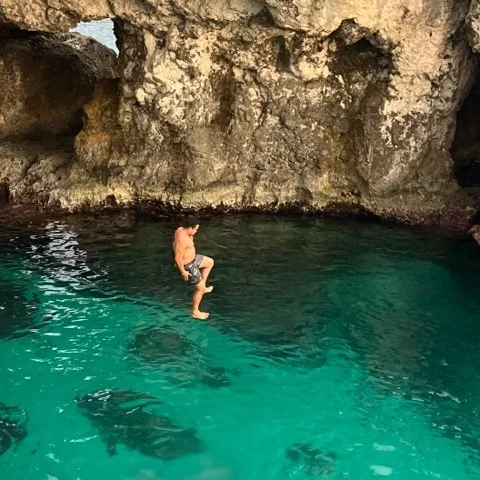 A man jumping from a cliff into clear water. 