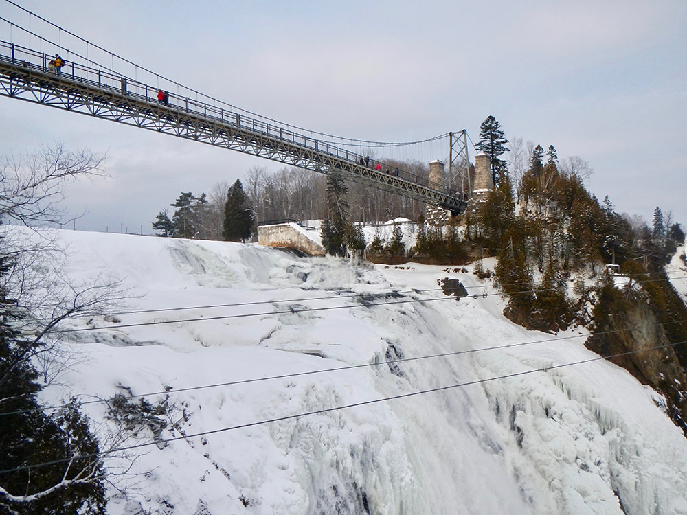 Frozen waterfall covered in snow with grey suspension bridge in Quebec City Canada