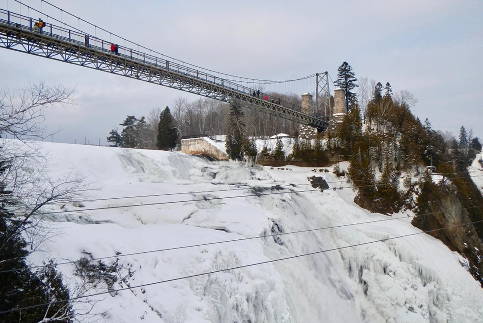 Frozen waterfall covered in snow with grey suspension bridge in Quebec City Canada