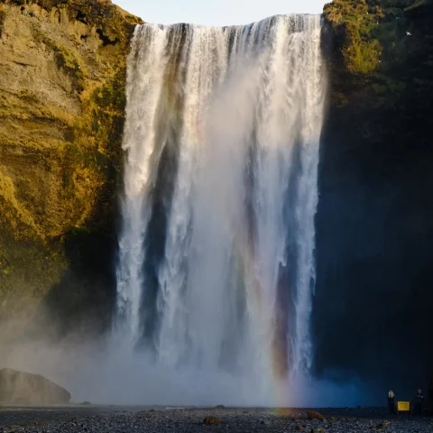 a waterfall onto black sand beach with a rainbow appearing from the pool below