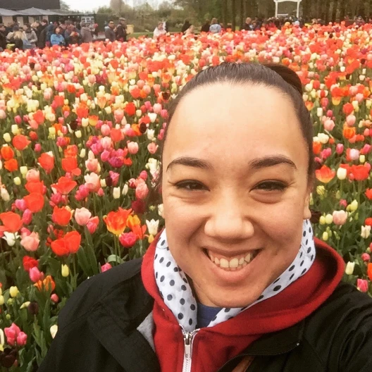 Fora travel advisor Elizabeth Callaway wearing red sweatshirt and black jacket stands in front of colorful field of tulips
