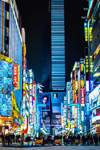 Tall buildings in Japan lit up by bright lights and signs with a crowded crosswalk