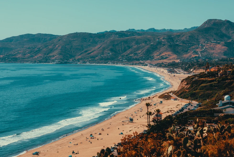 Beach with blue water and green hills.