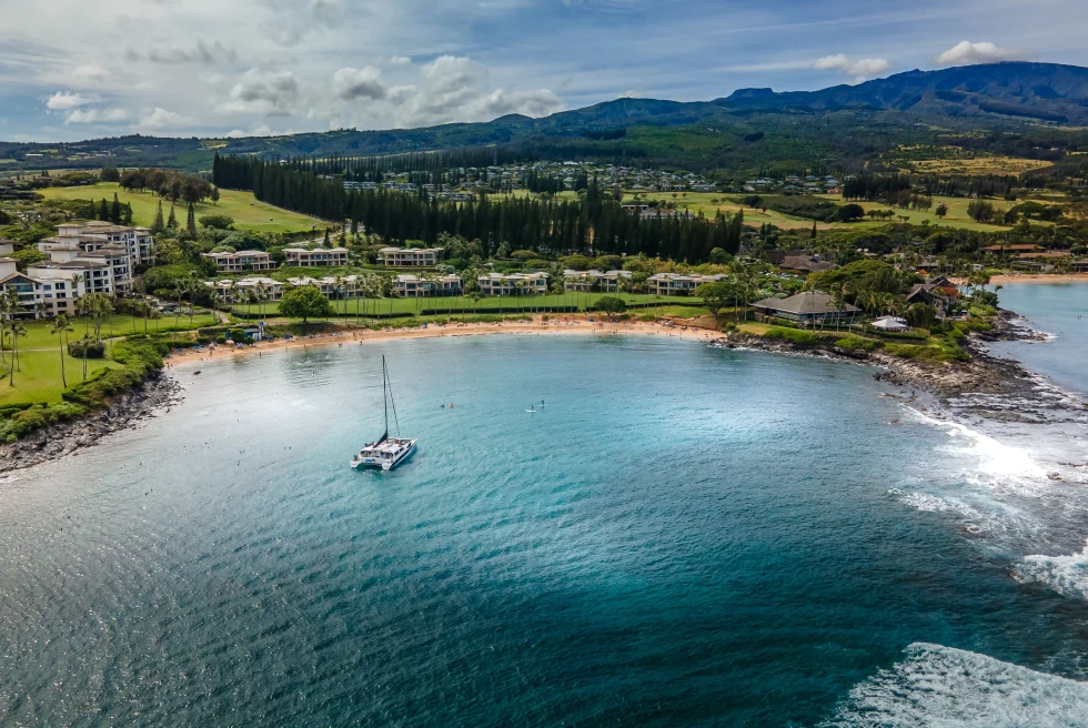 Aerial view of body of water with boat next to land with mountains during daytime