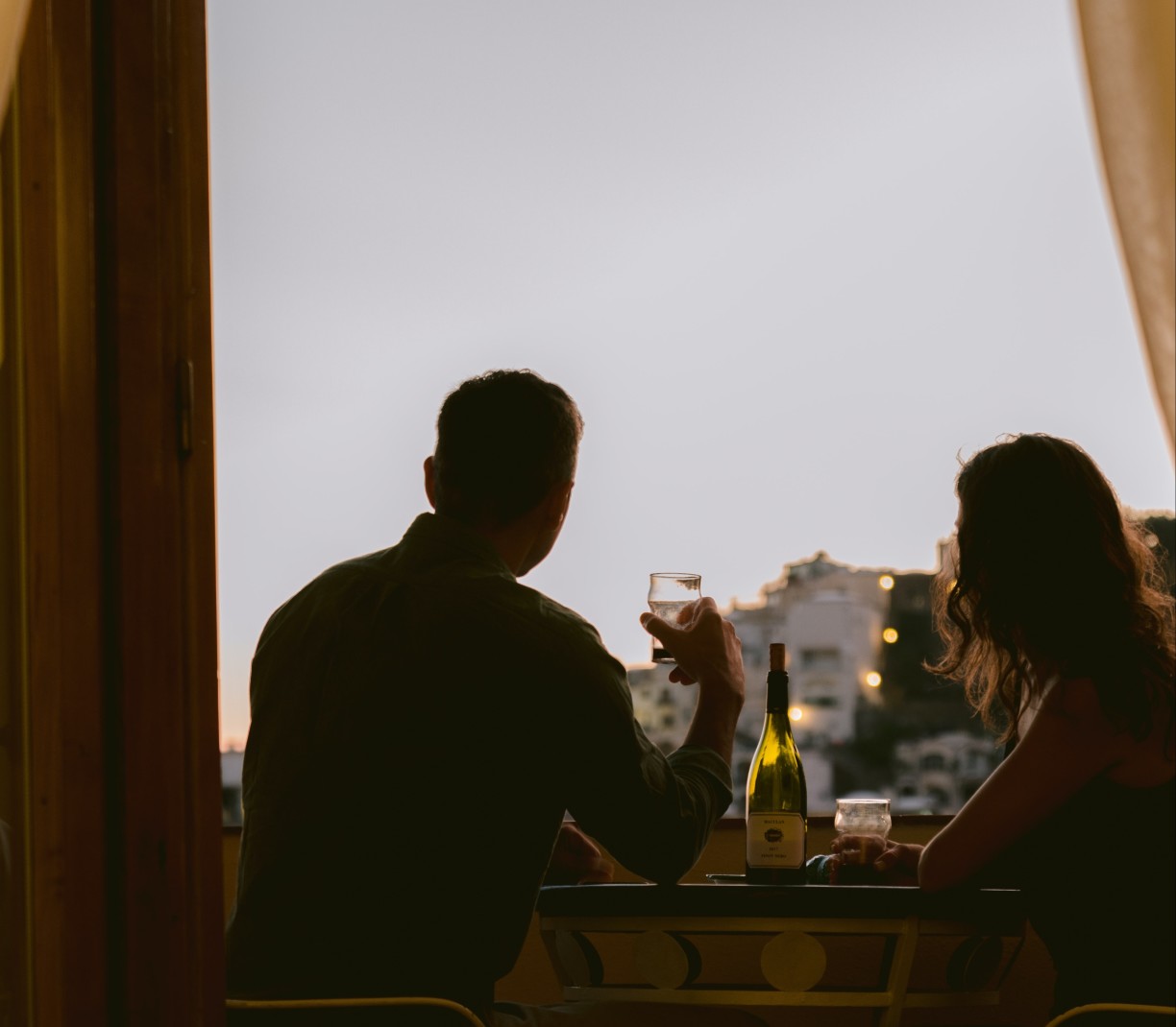 two people sitting at a bar holding glasses of wine