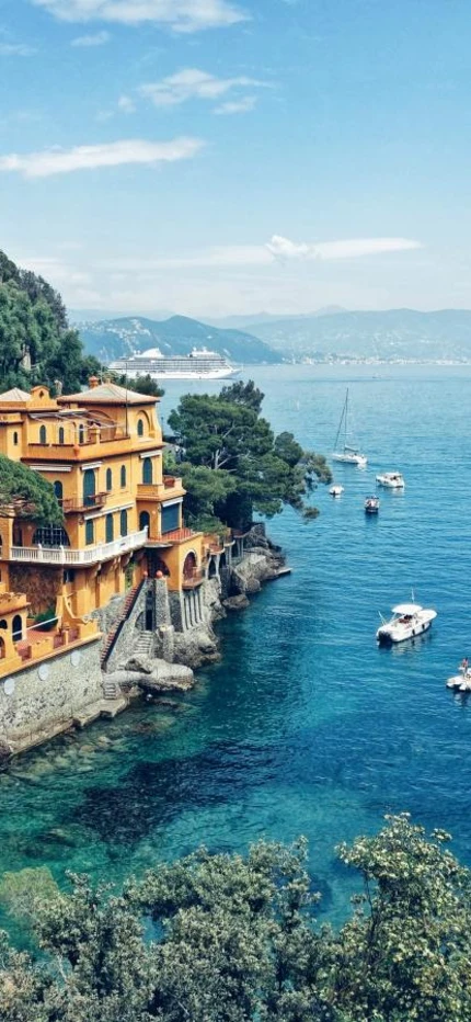 Sailboats in the blue waters and yellow and pink buildings along the coast of Italy in Portofino