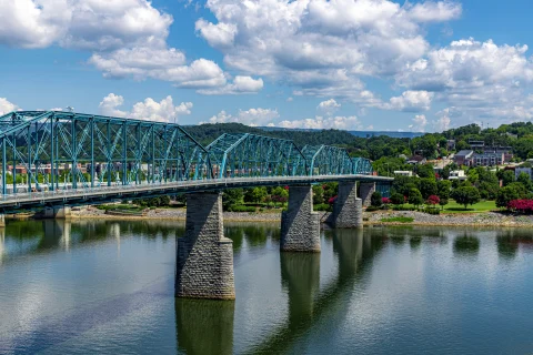 Bridge over blue water in Chattanooga, Tennessee leading to land with green grass and trees on a sunny day