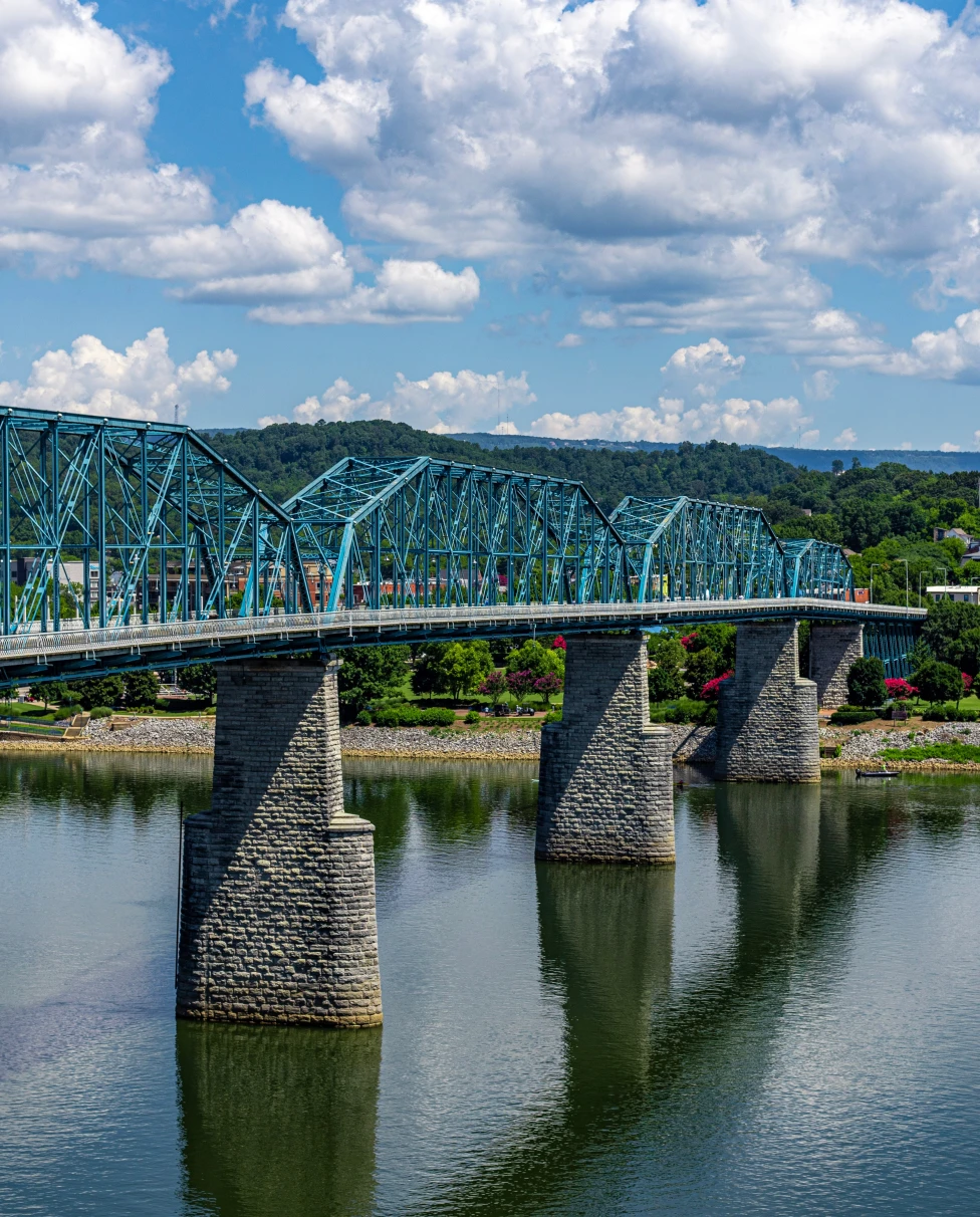 Bridge over blue water in Chattanooga, Tennessee leading to land with green grass and trees on a sunny day