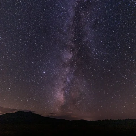 A view of a beautiful starry constellation at nighttime above a dark mountain top. 