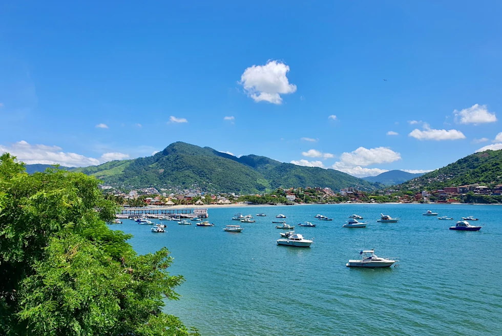 clear blue water in a harbor dotted by moored boats and rolling hills in the background