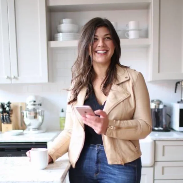 travel advisor Caitlin Bartram in a beige jacket and jeans standing in a kitchen
