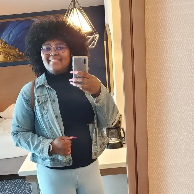 Travel Advisor Saronda Gray standing in a hotel room in a black turtleneck and jean jacket.