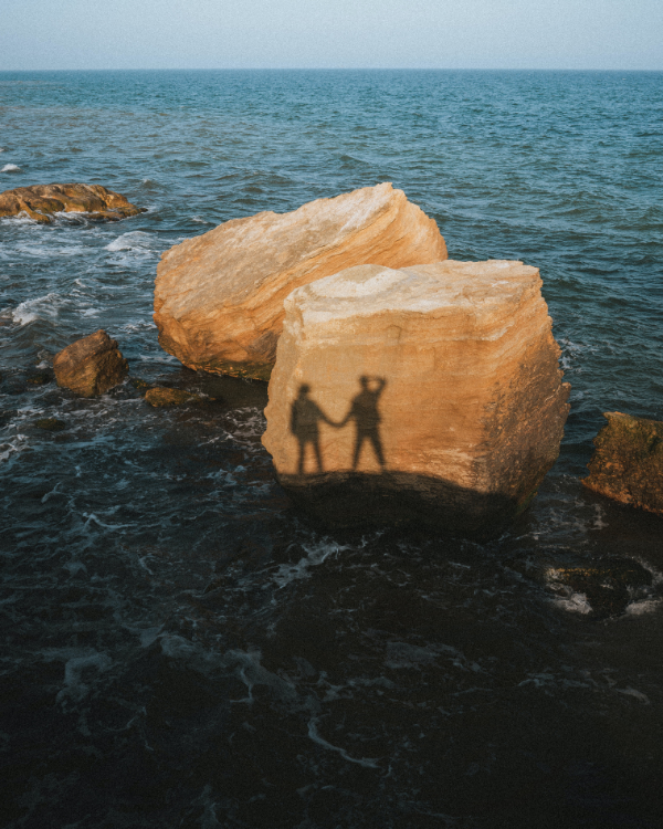 Silhouettes of couple holding hands against rocks in the ocean. 