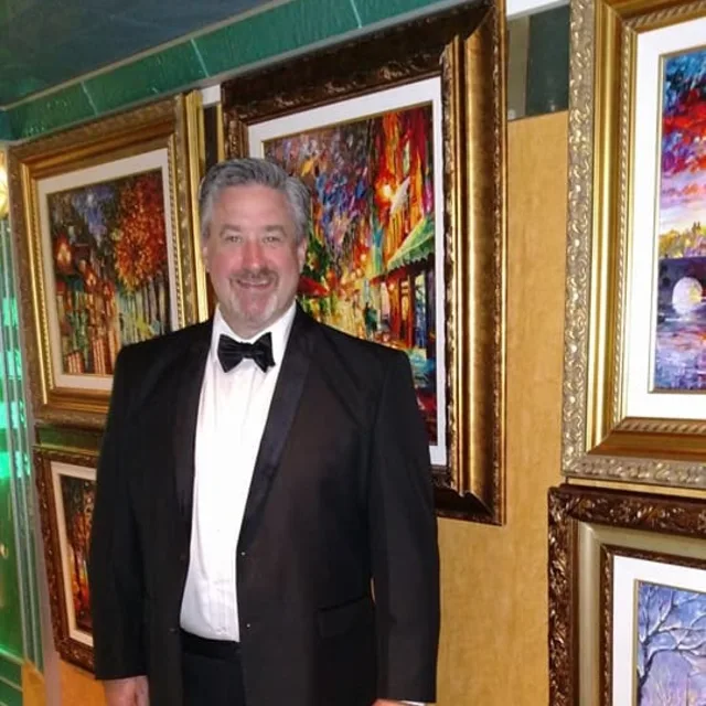 Travel Advisor Rich Carithers with a white and black tux standing in front of artwork.