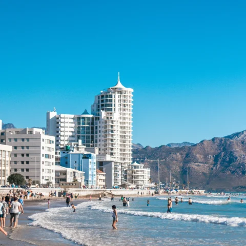cape town south africa beach and city view of white buildings with people in the waves brown cliffs and blue water