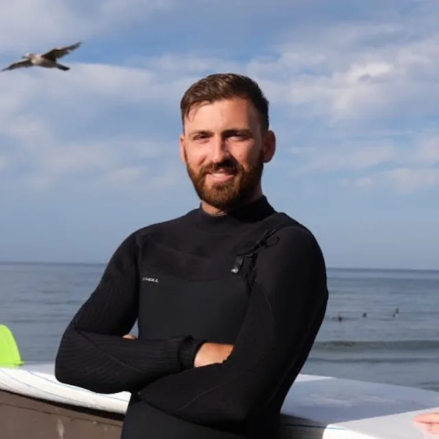 Travel Advisor Jake Adee in a wetsuit with a bird flying in the background and a large body of water.