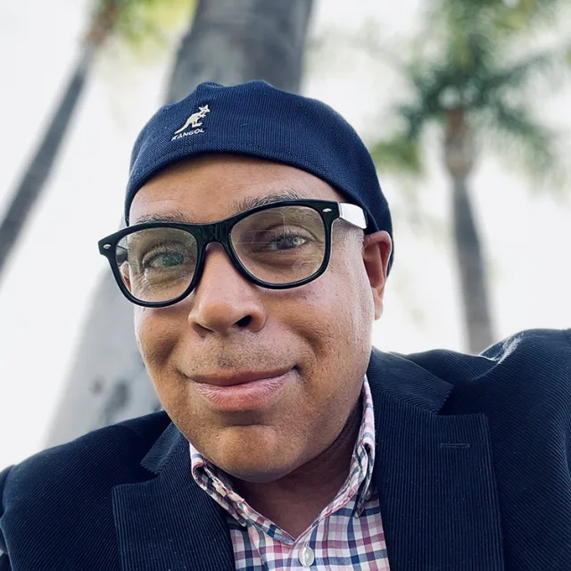 Fora travel agent Irving Macario wearing hat and glasses with palm tree in background