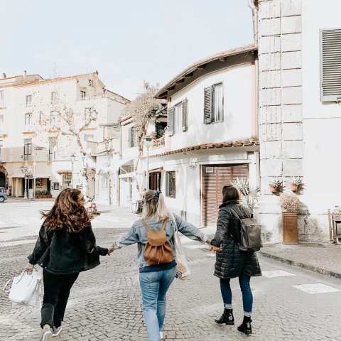A picture of three girls holding hands and walking on the street surrounded by white buildings.